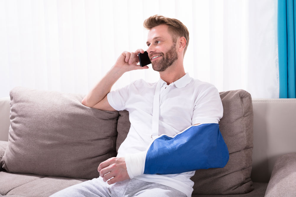 Man with broken arm sitting on couch talking on a cell phone